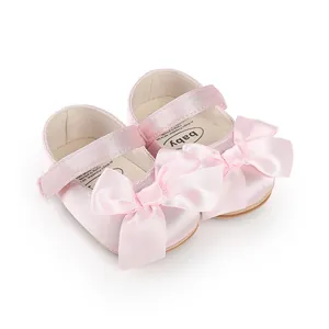 Close-up detail of soft pink satin baby pre-walker shoes featuring large elegant ribbon bows