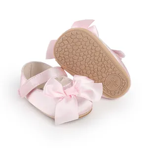Detailed view of pink satin baby pre-walker shoes featuring a large bow and anti-slip sole