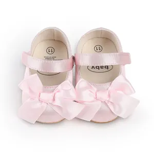 Close-up of pink satin baby walker shoes featuring large bows and adjustable straps