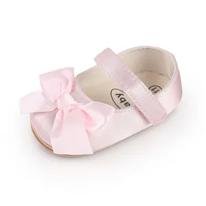 Close-up of pink satin baby walking shoe featuring a large decorative bow and strap.