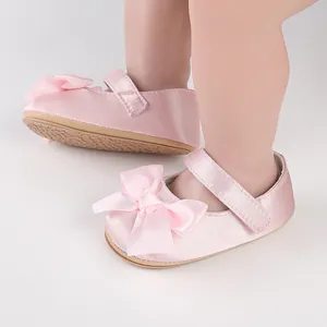 Detail view of pink satin baby walking shoes featuring a cute bow and velcro strap