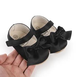 Detailed macro view of black satin baby walking shoes featuring large decorative bows