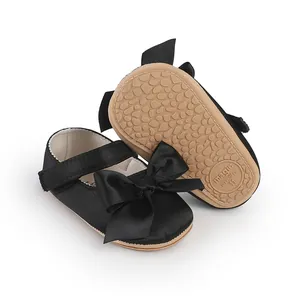 Detailed view of black satin infant walking shoes with a large bow and non-slip sole