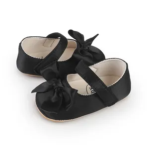 Detailed close-up of elegant black satin baby Mary Jane walking shoes with large decorative bows
