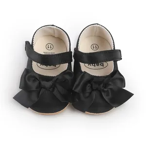 Top view of black satin baby walking shoes with large bows and Velcro straps