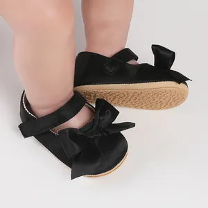 Detailed view of black satin infant walker shoes featuring an elegant bow-tie and rubber sole