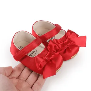 Red satin baby walking shoes with elegant big bows held in hand for close-up detail