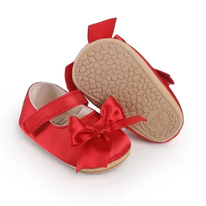 Red satin baby prewalker shoes featuring a large bow and a non-slip rubber sole detail view.