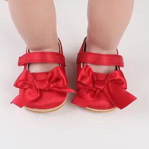 Detail view of red satin infant walking shoes featuring a large decorative bow and strap