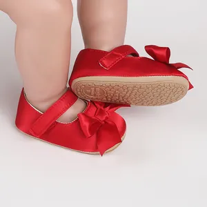 Detail view of red satin baby walker shoes with a decorative bow and textured anti-slip sole