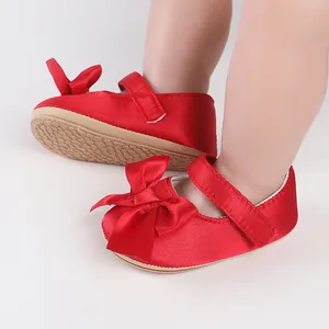 Detailed view of red satin baby walking shoes with a large bow and non-slip sole.