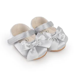 Silver satin baby prewalker shoes with a large decorative bow and easy Velcro strap.