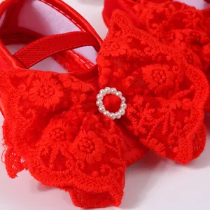 Close-up of red baby princess shoe featuring a large lace bow and pearl buckle detail.