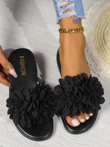 Dettaglio di ciabatte nere da donna con grandi decorazioni floreali in tessuto 3D.