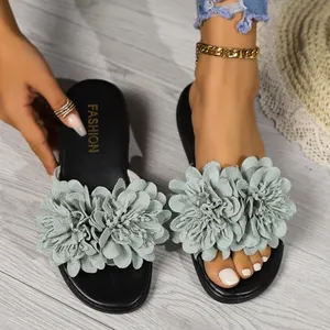 Dettaglio di ciabatte piatte da donna con fiori decorativi in tessuto verde chiaro.