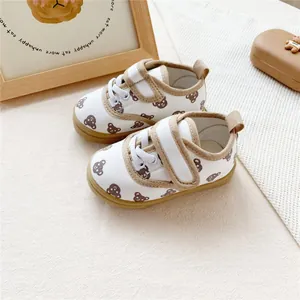 Close-up view of white baby canvas shoes with brown bear patterns and secure velcro straps.