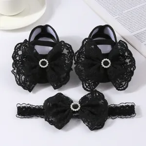 Detail view of black lace baby shoes and matching headband set with large bows.