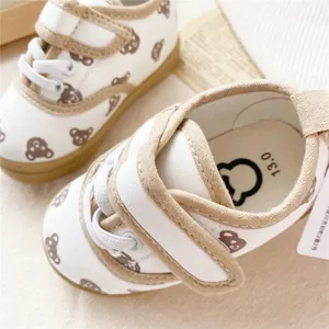 Close-up detail of white kids canvas shoes with brown bear pattern and velcro strap.