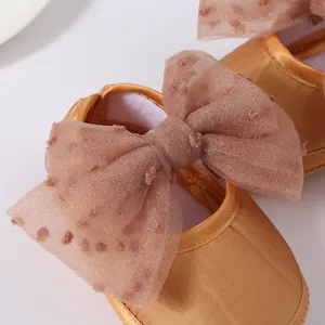 Primer plano de zapatos de princesa dorados para bebé con un lazo de tul rosa con lunares.
