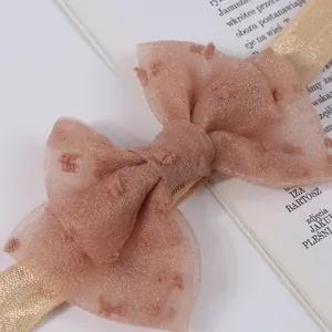 Primer plano detallado de una diadema para bebé con lazo rosa y cinta elástica dorada