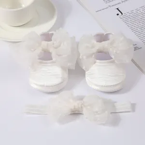 Detalle de zapatos de princesa para bebé blancos y diadema con lazo a juego