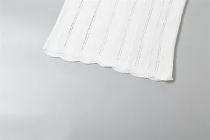 Close-up detail of white knitted dress showing scalloped hem and pointelle texture