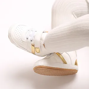 Close-up of white baby walking shoes with gold stripes and soft brown sole