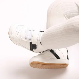Close-up detail of white soft-sole baby sneakers featuring black stripes and a velcro strap
