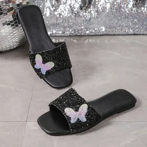 Dettaglio di ciabatte nere glitterate con decorazione a farfalla colorata