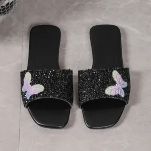 Dettaglio di ciabatte piatte con paillettes nere e decorazioni a farfalla in strass vivaci