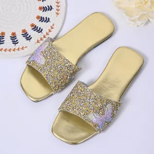 Dettaglio di ciabatte piatte dorate con paillettes e decorazione a farfalla in strass.