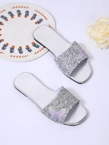 Primo piano di sandali piatti con paillettes argento e decorazione a farfalla.