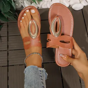 Sandalias planas marrones de verano para mujer con detalle ovalado de metal en una terraza