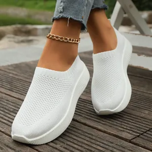 Close-up detail of white fly-knit breathable mesh casual sneakers on a wooden surface