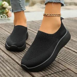 Close-up detail of black breathable knitted mesh slip-on sneakers worn on a foot outdoors