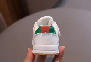 Detail view of white toddler sneakers with green and orange heel accents and durable sole