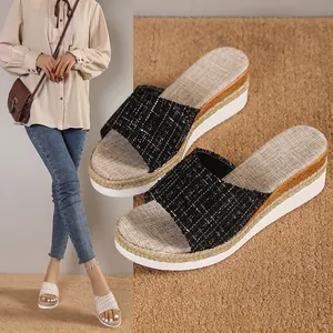 Gros plan de sandales compensées noires en tweed avec semelle tressée et bordure dorée.