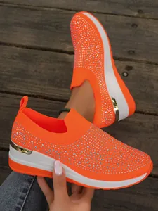 Dettaglio scarpe sneaker con zeppa arancione neon con strass e suola platform bianca.