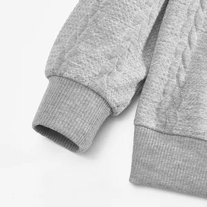 Detail eines grauen schweren Jacquard-Sweatshirts mit Rippbündchen und Flechtstruktur
