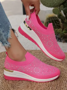 Dettaglio di sneaker con zeppa rosa, decorata con strass e tessuto a rete traspirante.