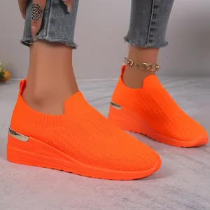 Close-up of bright orange breathable knitted wedge sneakers with metallic heel detail