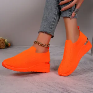 Detail of vibrant orange fly-knit wedge sneakers shown on a model with denim jeans.