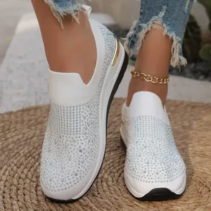 Primo piano di sneakers slip-on bianche da donna con strass e zeppa spessa su tappeto