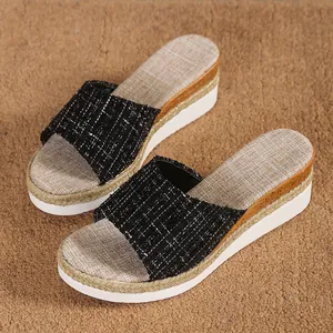Détail de sandales compensées pour femmes avec bride en tweed noir et bordure tressée.
