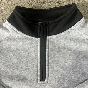 Detailopname van een grijs fleece sweatshirt met zwarte opstaande kraag en halve rits.