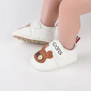 Dettaglio di scarpine bianche per primi passi con orsetto e chiusura in velcro.