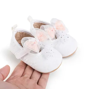 Detailed view of white baby walking shoes featuring pink lace bows held in hand