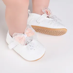 Close-up detail of white baby walking shoes with a decorative pink lace bow decoration
