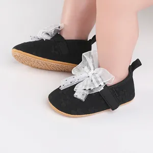Close-up detail of black baby walking shoes featuring an elegant white lace bow for infants