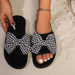 Dettaglio di eleganti ciabatte piatte nere con fiocco decorativo a quadretti vichy.